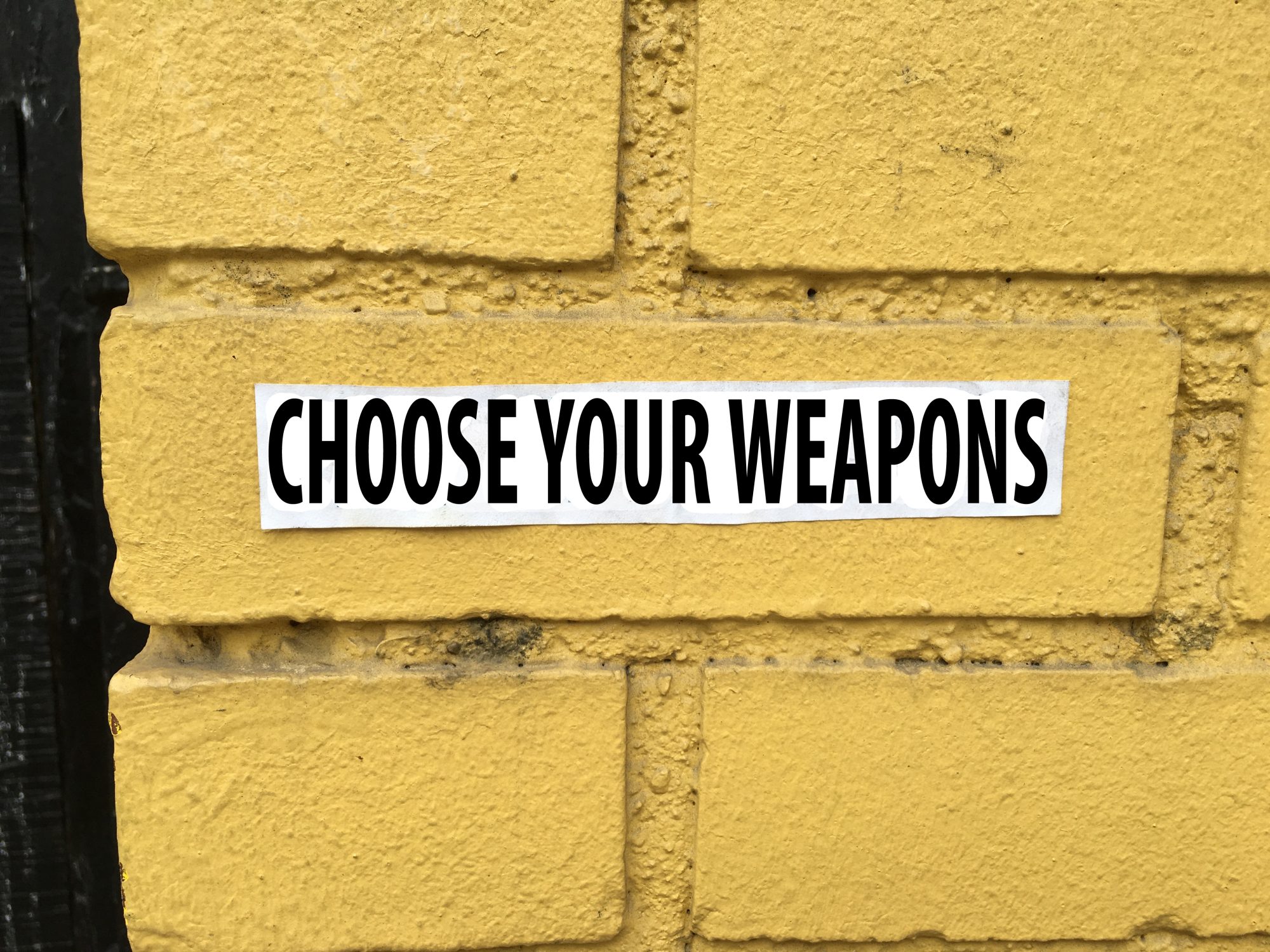 yellow brick wall with text choose your weapons for blog post at sandyhibbardcreative.com
